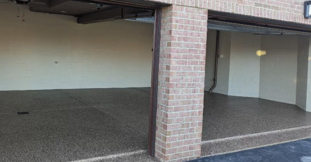 A clean, empty garage with two open doors, featuring brick exterior and speckled flooring, illuminated by natural light from outside.