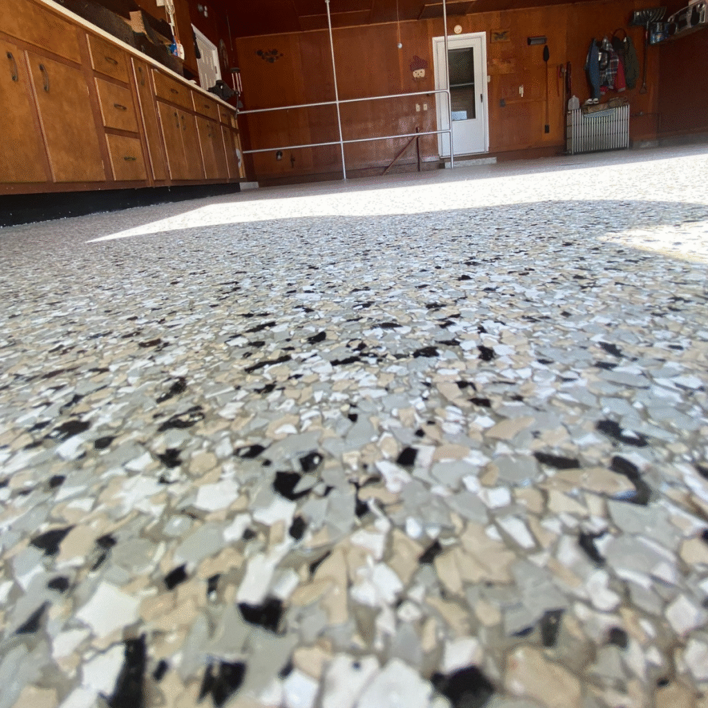 Close-up of a terrazzo floor in a garage, with warm brown cabinets, assorted wall hangings, and a door visible in the background.