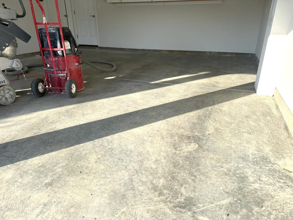 A shadow-filled garage features a red trolley, vacuum, and concrete floor. Organized shelves are visible on the back wall.