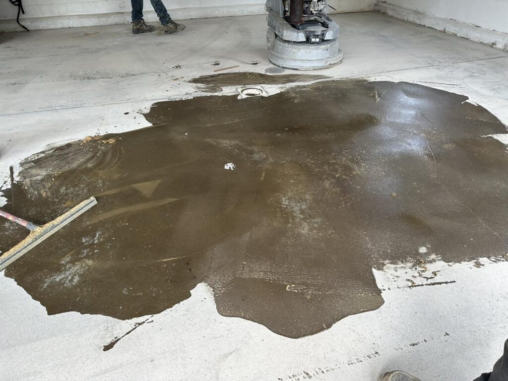 A person works on polishing a brown, wet concrete floor with a machine in an indoor construction setting.
