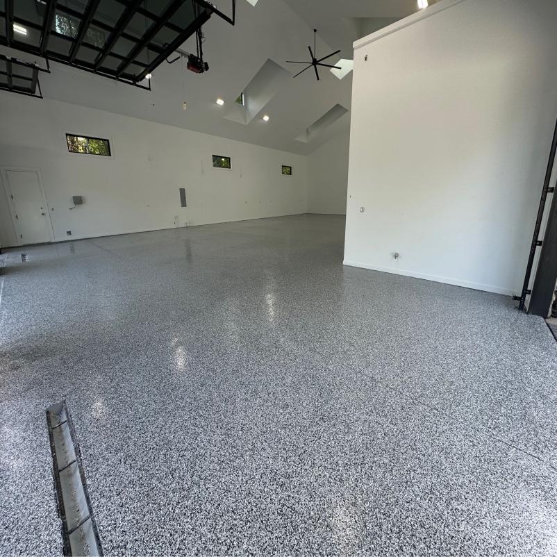 Spacious, empty white room with polished speckled floor, high ceiling, skylights, and industrial-style garage doors. Modern, minimalist interior design.