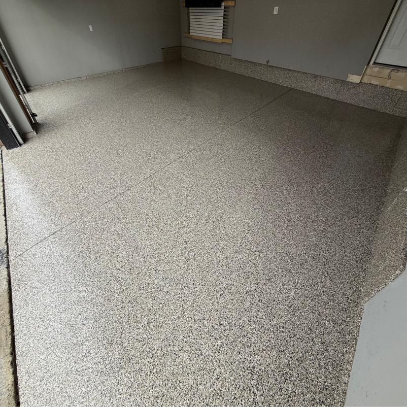 Polished epoxy garage floor with speckled design in a spacious, empty garage. Plain walls and a small window are visible.