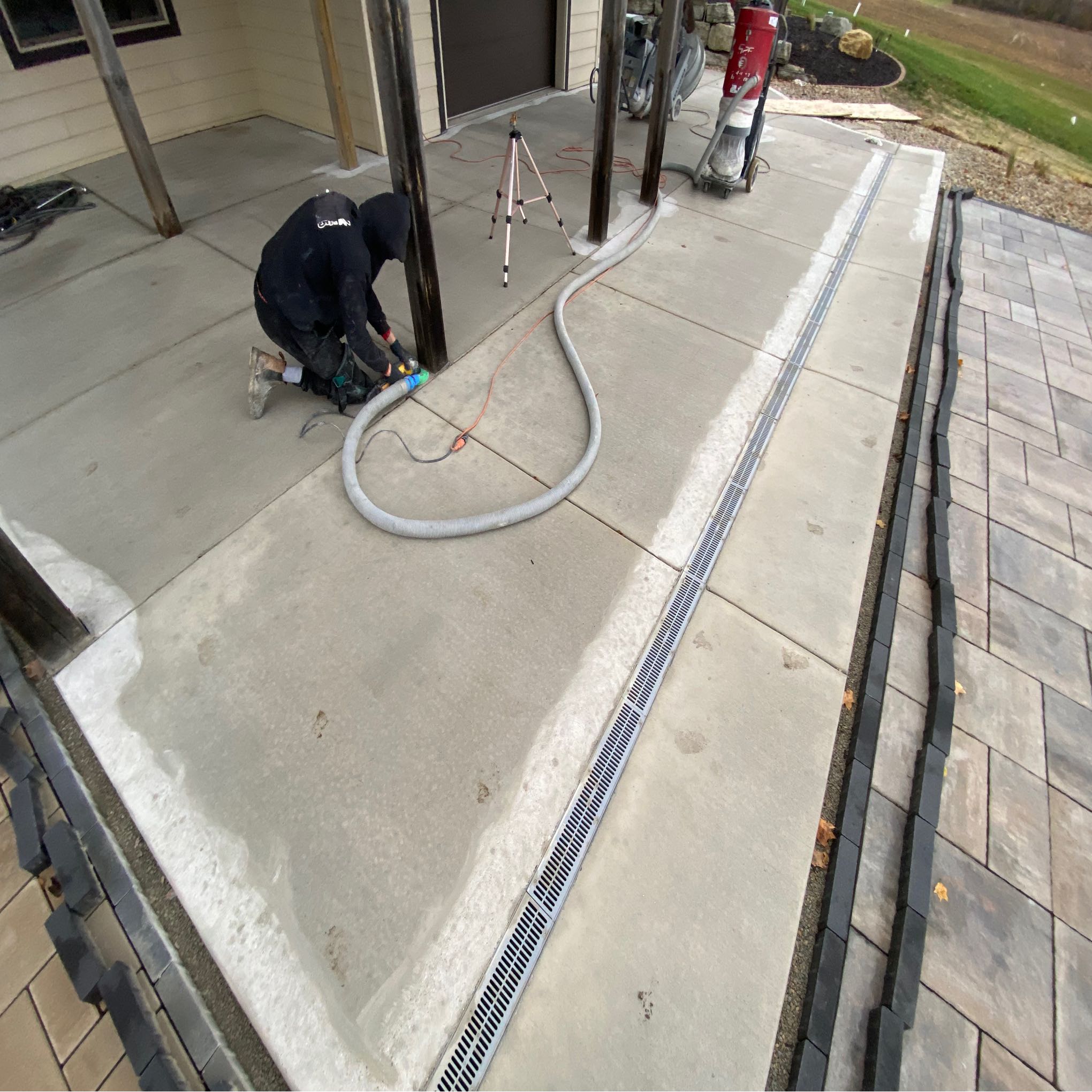 A person works on concrete near a house with tools and a hose, focusing on surface improvements in an outdoor setting.